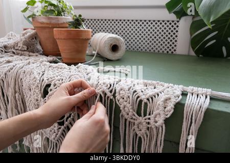le mani delle donne tessono pannelli in macrame. fili di cotone, filati per la fabbricazione di prodotti fatti a mano per interni. Foto Stock
