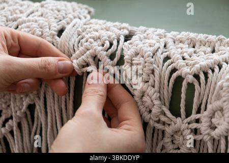 le mani delle donne tessono pannelli in macrame. fili di cotone, filati per la fabbricazione di prodotti fatti a mano per interni. Foto Stock
