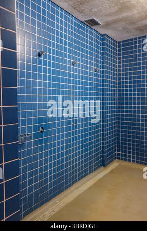 Interno di una moderna sala doccia pubblica con piastrelle blu e scarico a pavimento. Foto Stock