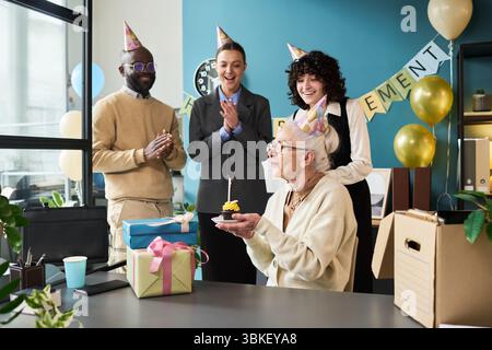 Donna caucasica anziana che soffia la candela su Cupcake durante la riunione di pensionamento Foto Stock