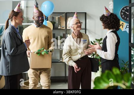 Donna caucasica anziana che si impegna con diversi colleghi durante l'evento di pensionamento Foto Stock