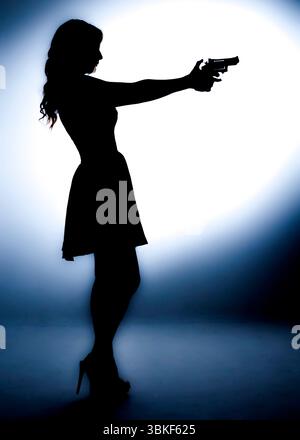 Una donna con la silhouette tiene in mano una pistola, puntandola in avanti. L'immagine è illuminata da una luce brillante dietro di lei, creando un effetto drammatico. Foto Stock