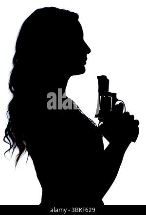La silhouette di una donna che tiene in mano una pistola, che suggerisce una scena di potenziale pericolo o azione. Foto Stock