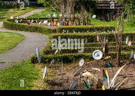 Piatti su pali in un giardino frontale in Francia, Nouvelle-Aquitaine. Il motivo si inserisce nel proverbio tedesco "Über den Tellerrand schauen" (guarda oltre il bordo del piatto), che si riferisce a un atteggiamento aperto e curioso in cui si è disposti a trascendere i propri confini e ad imparare cose nuove. La frase è spesso usata in connessione con il cosmopolitismo, un cambiamento di prospettiva o innovazione. Pensare fuori dagli schemi. L'installazione decorativa del giardino comprende vari pezzi di stoviglie attaccati ai bastoncini e collocati in un letto di fiori per creare una scena giocosa e artistica. L'installazione è Foto Stock