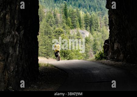 Una donna fa un giro in bicicletta attraverso il Little Tunnel sul KVR, il percorso ferroviario Kettle Valley vicino a Naramata, nell'Okanagan, Columbia Britannica, Canada Foto Stock