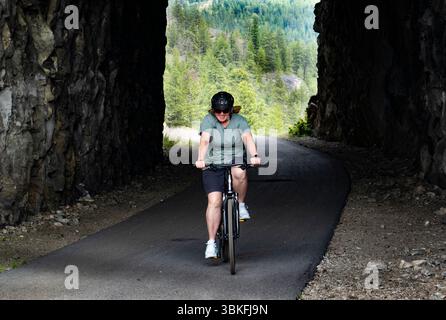 Una donna fa un giro in bicicletta attraverso il Little Tunnel sul KVR, il percorso ferroviario Kettle Valley vicino a Naramata, nell'Okanagan, Columbia Britannica, Canada Foto Stock