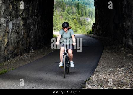 Una donna fa un giro in bicicletta attraverso il Little Tunnel sul KVR, il percorso ferroviario Kettle Valley vicino a Naramata, nell'Okanagan, Columbia Britannica, Canada Foto Stock