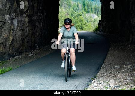 Una donna fa un giro in bicicletta attraverso il Little Tunnel sul KVR, il percorso ferroviario Kettle Valley vicino a Naramata, nell'Okanagan, Columbia Britannica, Canada Foto Stock