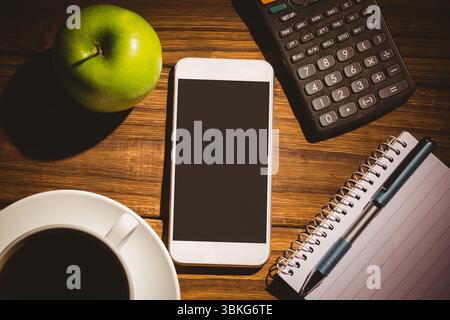 Scrivania piatta con smartphone bianco con mela verde, caffè, calcolatrice, notebook e penna Foto Stock