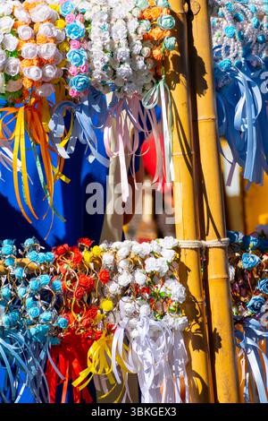 Corone di fiori colorate in vendita in un tradizionale mercato di strada. Accessori per il festival estivo con rose e nastri. Foto Stock
