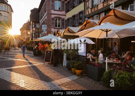 Ribeauvillé, Alsazia, Francia: Ospiti sulla terrazza della Brasserie la Post nel vicolo medievale con case a graticcio retroilluminate dal tramonto Foto Stock