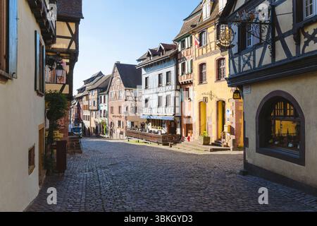 Case colorate e in legno lungo la strada principale nella tranquilla città vecchia di Riquewihr, al sole della mattina presto, in Alsazia, Francia Foto Stock