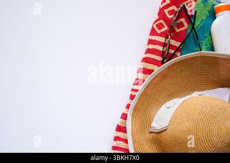 Cappello di paglia e occhiali da sole su sfondo bianco con telo da bagno e crema solare, vacanze estive, foto di nuoto Foto Stock