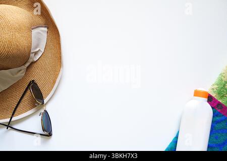 Cappello di paglia e occhiali da sole su sfondo bianco con telo da bagno e crema solare, vacanze estive, foto di nuoto Foto Stock