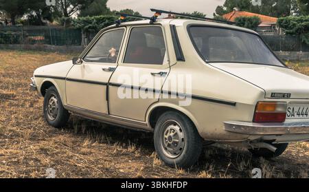 Una classica Renault 12 beige è parcheggiata in un campo arido e arido con una casa e alberi visibili sullo sfondo. La vettura ha un design distintivo Foto Stock