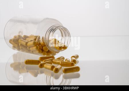 Un vaso con le pillole all'interno giace su uno sfondo bianco. Acido ialuronico, collagene, vitamine o mirtillo per perdere peso. Preparazioni mediche per la salute Foto Stock