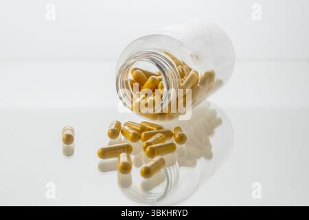 Un vaso con le pillole all'interno giace su uno sfondo bianco. Acido ialuronico, collagene, vitamine o mirtillo per perdere peso. Preparazioni mediche per la salute Foto Stock