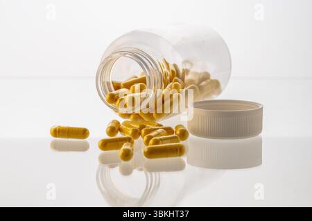 Un vaso con le pillole all'interno giace su uno sfondo bianco. Acido ialuronico, collagene, vitamine o mirtillo per perdere peso. Preparazioni mediche per la salute Foto Stock
