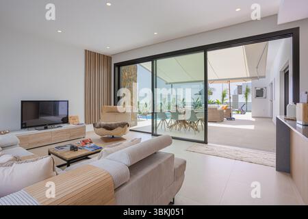 Soggiorno con porte scorrevoli in vetro che si aprono sulla terrazza con piscina e zona pranzo. Foto Stock
