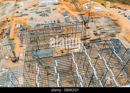 I lavoratori stanno assemblando grandi strutture in acciaio in cantieri edili affollati e circondati da materiali. Foto Stock
