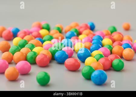latte sparsi, vivace e colorato, caramelle o ciottoli ricoperti di dolci su sfondo grigio, primo piano di snack dolciumi con messa a fuoco morbida e spazio di copia Foto Stock
