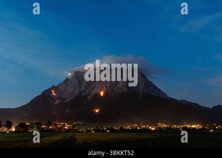 Lermoos, Austria. 21 giugno 2025, Austria, Lermoos: Numerosi incendi si possono vedere sulle montagne nella Tirolo Zugspitz Arena nel bacino Ehrwald Lermoos e Biberwier nel Tirolo (Austria) il 21.06.2025 per il solstizio d'estate. L'immagine mostra i monti Wetterstein con il lato tirolese dello Zugspitze, su cui sono bruciati motivi come una croce, un alfa e un omega, una colomba di pace e una marmotta. Ogni anno, il giorno più lungo e la notte più breve della regione sono celebrati con spettacolari motivi di fuoco a testimonianza di questa tradizione. Credito: dpa Picture Alliance/Alamy Live News Foto Stock
