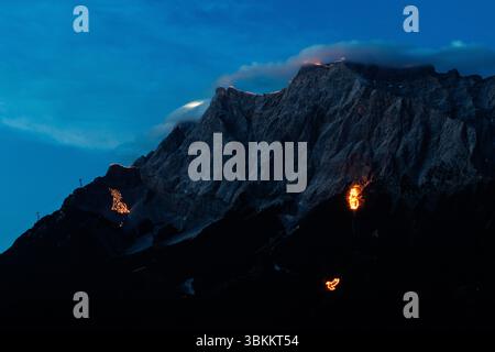 Lermoos, Austria. 21 giugno 2025, Austria, Lermoos: Numerosi incendi si possono vedere sulle montagne nella Tirolo Zugspitz Arena nel bacino Ehrwald Lermoos e Biberwier nel Tirolo (Austria) il 21.06.2025 per il solstizio d'estate. L'immagine mostra i monti Wetterstein con il lato tirolese dello Zugspitze, su cui sono bruciati motivi come una croce, un alfa e un omega, una colomba di pace e una marmotta. Ogni anno, il giorno più lungo e la notte più breve della regione sono celebrati con spettacolari motivi di fuoco a testimonianza di questa tradizione. Credito: dpa Picture Alliance/Alamy Live News Foto Stock