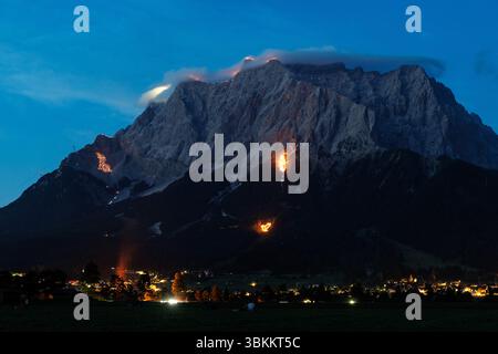 Lermoos, Austria. 21 giugno 2025, Austria, Lermoos: Numerosi incendi si possono vedere sulle montagne nella Tirolo Zugspitz Arena nel bacino Ehrwald Lermoos e Biberwier nel Tirolo (Austria) il 21.06.2025 per il solstizio d'estate. L'immagine mostra i monti Wetterstein con il lato tirolese dello Zugspitze, su cui sono bruciati motivi come una croce, un alfa e un omega, una colomba di pace e una marmotta. Ogni anno, il giorno più lungo e la notte più breve della regione sono celebrati con spettacolari motivi di fuoco a testimonianza di questa tradizione. Credito: dpa Picture Alliance/Alamy Live News Foto Stock