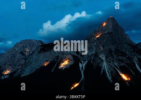 Lermoos, Austria. Lermoos, Austria. 21 giugno 2025. Numerosi fuochi si possono vedere sulle montagne nella Tirolese Zugspitz Arena nel bacino della valle Ehrwald Lermoos e Biberwier in Tirolo (Austria) il 21.06.2025 per il solstizio d'estate. L'immagine mostra l'Ehrwalder Sonnenspitze nel Mieminger Kette. Ogni anno, il giorno più lungo e la notte più breve vengono celebrati nella regione con spettacolari fuochi d'artificio. All'imbrunire, il cosiddetto "Bergfeurer" accende gli incendi di mezza estate, che poi bruciano nella notte. Credito: dpa Picture Alliance/Alamy Live News Foto Stock