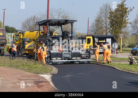 I lavoratori della costruzione di strade utilizzano macchinari pesanti per posare asfalto fresco in una giornata di sole, migliorando le infrastrutture stradali in un'area rurale. Utrecht, Paesi Bassi Foto Stock