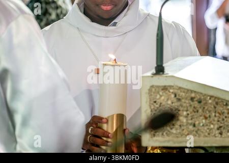 Una persona che tiene in mano una candela pasquale illuminata durante una cerimonia di battesimo cristiano, simboleggiando la luce, il rinnovamento e la fede spirituale. Foto Stock