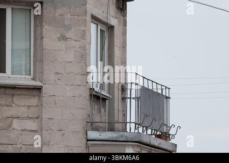 Vista ravvicinata della facciata di un edificio in pietra con una ringhiera in metallo arrugginito che mostra il decadimento urbano e l'invecchiamento, ideale per temi di abbandono Foto Stock