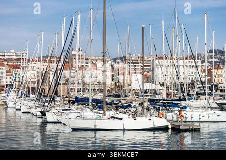 Cannes, Francia - 8 marzo 2025: Barche da pesca e yacht nel Porto Vecchio con Palais des Festivals e colline cittadine sullo sfondo. Foto Stock