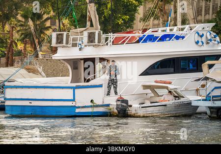 Cairo, Egitto - 11 settembre 2023: Yacht ormeggiato sul Nilo al Cairo, Egitto, con una guardia in uniforme dell'esercito egiziano, piccole barche e fiumi lussureggianti Foto Stock