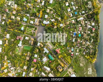 Una vista aerea dall'alto verso il basso che cattura il layout residenziale di Serebryansk, Kazakistan, con case, spazi verdi e alberi autunnali vicino al fiume Foto Stock