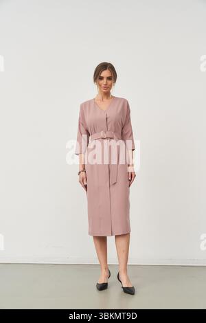 Elegante donna dallo stile minimalista, indossa un abito al ginocchio con cintura e maniche a tre quarti e scarpe nere. I suoi capelli sono modellati con cura Foto Stock