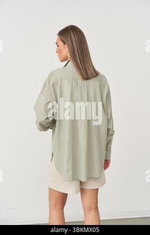 Persona dai capelli medi rivolta verso l'esterno, indossa una camicia a maniche lunghe verde chiaro e pantaloncini beige. La persona sta su un liscio Foto Stock