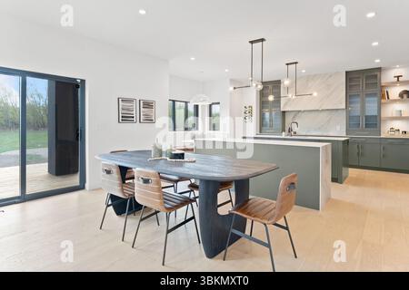 Un grande tavolo da pranzo e' circondato da sedie in una cucina moderna. Il tavolo è allestito con una bottiglia e una ciotola e sul tavolo sono presenti due vasi. La k Foto Stock