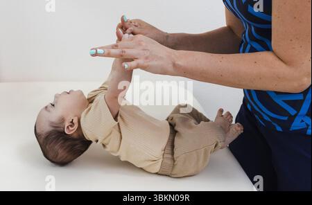 Fisioterapista che lavora con il neonato durante l'esame neurologico pediatrico per il test sui riflessi del neonato. Tirare per sedersi o per eseguire il test di trazione del braccio Foto Stock