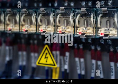 Un cartello di avvertimento giallo e nero è appeso su un muro. Il segnale è posizionato in una fila di prese elettriche, a indicare un potenziale pericolo. Il segno è posi Foto Stock