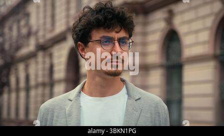 Primo piano ritratto bel millenario europeo pensivo serio calmo anni '30 ragazzo con gli occhiali che guardano intorno in piedi in città elegante uomo d'affari fiducioso Foto Stock