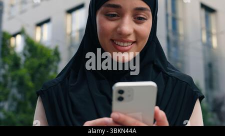 Ritratto felice sorridente musulmana positivo donna islamica che indossa hijab donna d'affari donna d'affari in città all'aperto in centro utilizzando il telefono cellulare Foto Stock