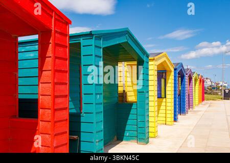 Una vivace fila di colorate capanne da spiaggia dipinte in rosso, verde, giallo, blu e cielo azzurro soleggiato lungo il mare, seaton carew, co. durham uk Foto Stock