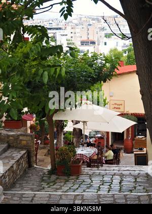 Vivace ristorante all'aperto sotto ombrelloni bianchi a Plaka, Atene, Grecia, con persone che cenano in un ambiente ombreggiato dagli alberi. Foto Stock
