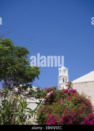 Torre bianca della chiesa con accenti blu chiaro in un villaggio mediterraneo circondato da bouganville, pini e vegetazione. Foto Stock