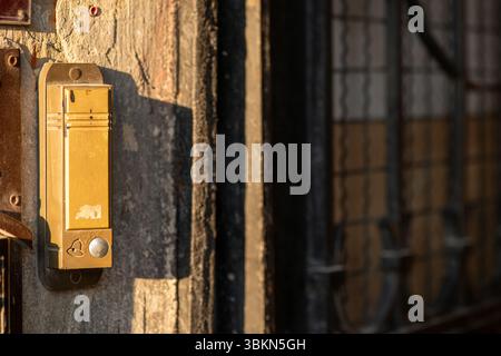 Un citofono dorato retrò su un muro di pietra ruvida con sfondo sfocato in luce solare calda Foto Stock
