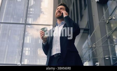 Uomo d'affari uomo d'affari sorridente uomo felice che parla telefono cellulare tenendo il caffè in città spensierato imprenditore maturo che parla vicino all'ufficio Foto Stock