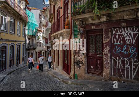 Una strada stretta e collinare nel centro storico di Porto. Gli edifici sono degradati e ricoperti di graffiti. Foto Stock