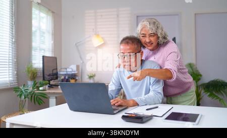 Felice coppia asiatica più anziana che usa un notebook a casa. Fanno shopping online e trascorrono del tempo insieme. Momento positivo della vita in pensione insieme Foto Stock