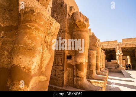 Fila di colossali statue di arenaria al tempio di Karnak a Luxor, Egitto, con dettagliati geroglifici e l'antica arte egizia alla luce del sole. Foto Stock
